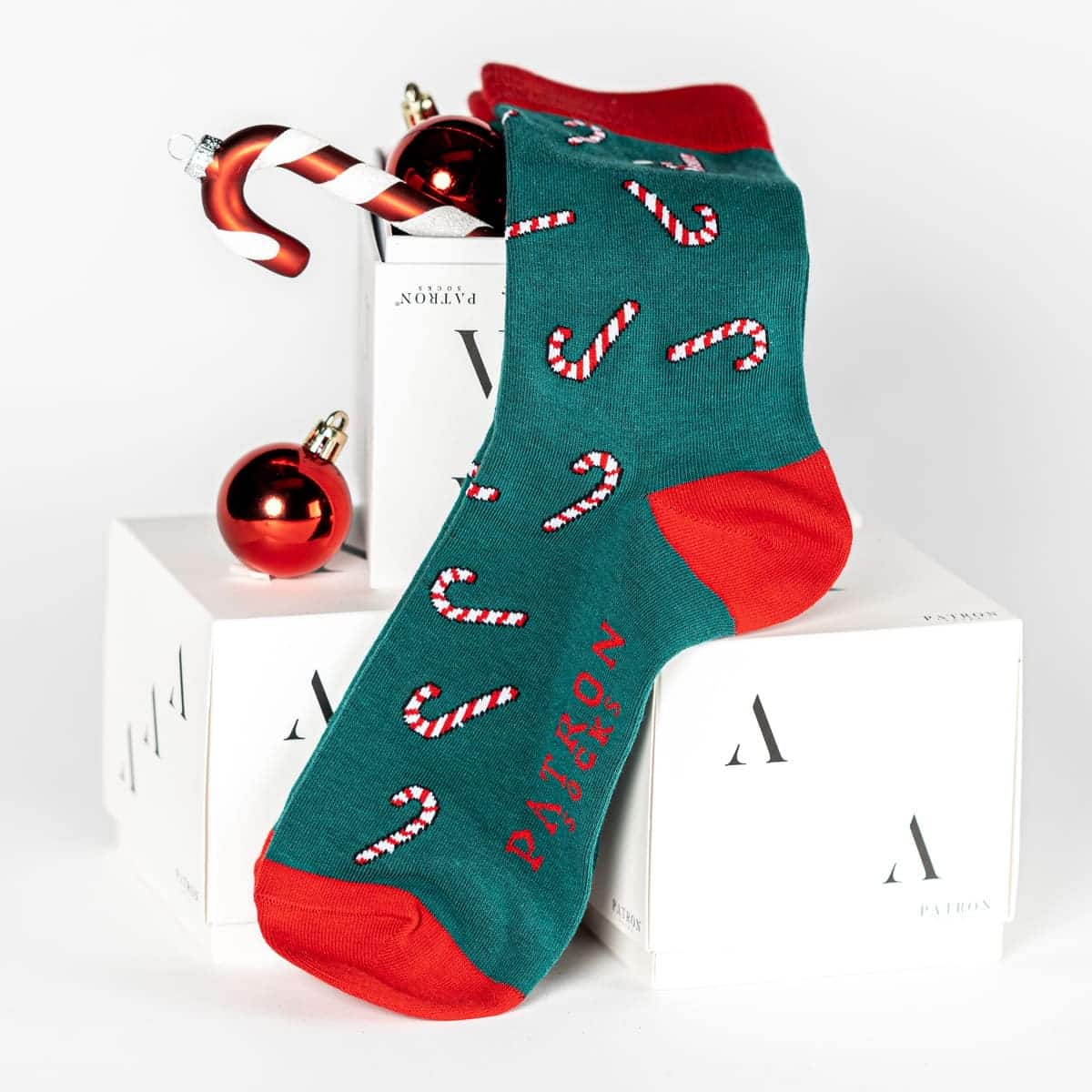 Eine mit Weihnachtskugeln dekorierte Box und grüne Zuckerstangen Socken von PATRON SOCKS