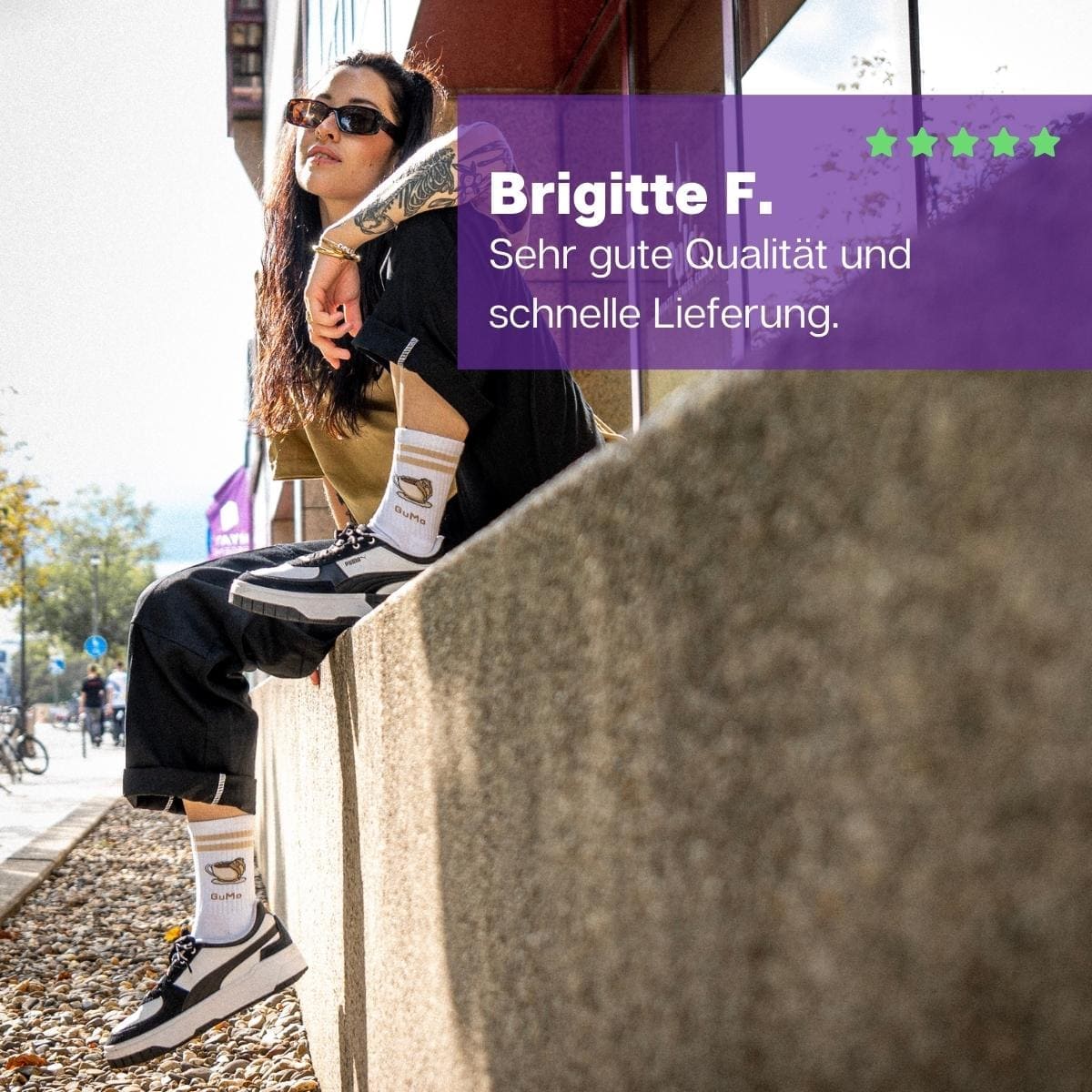 Frau mit schwarz-weißen Turnschuhen auf Mauer sitzend mit halbhohen weißen Sportsocken und GuMo Motiv von PATRON SOCKS