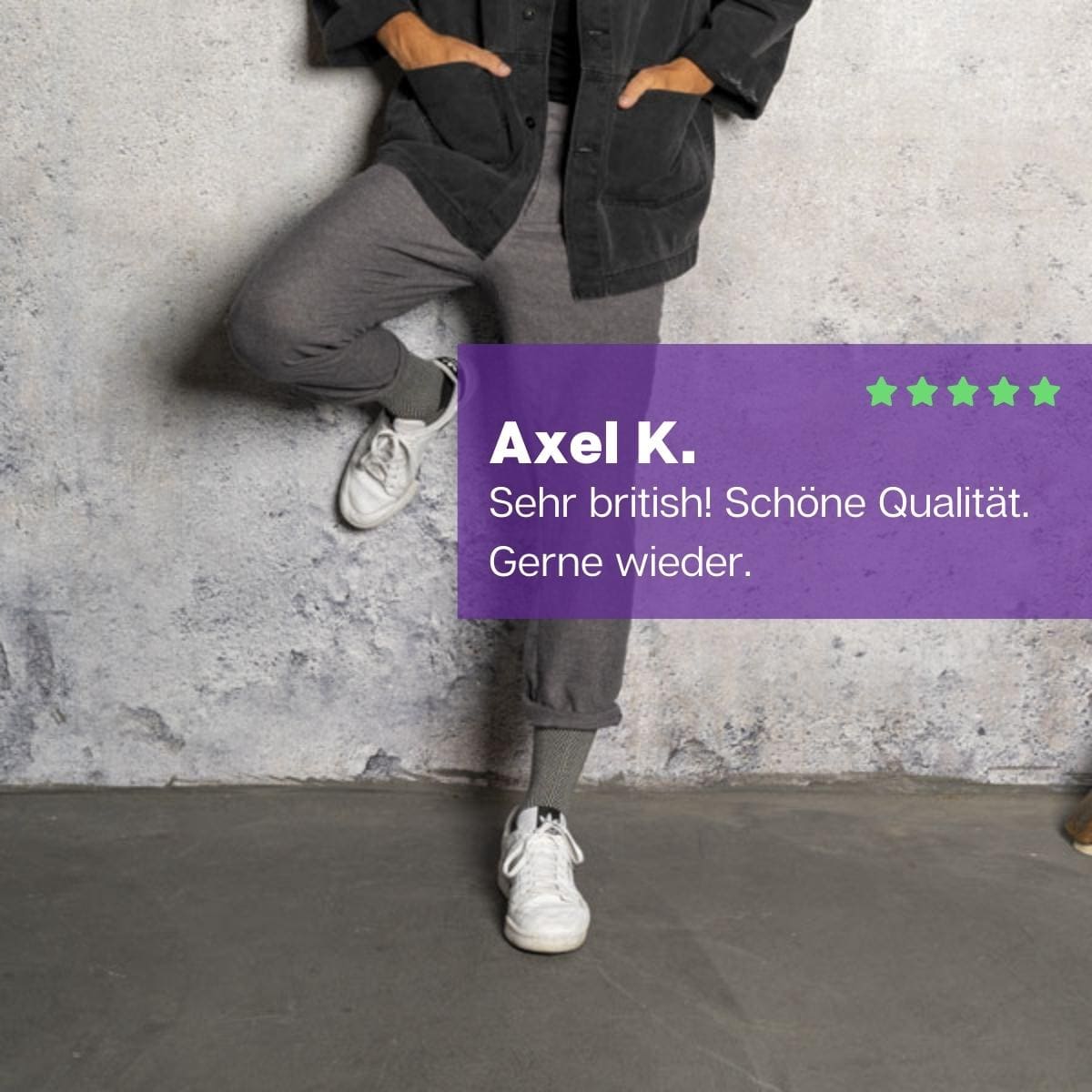Mann an einer Mauer stehend, bekleidet mit grauer Hose, weißen Sneakern und schwarz-weißen Luxus Herren Socken von PATRON SOCKS
